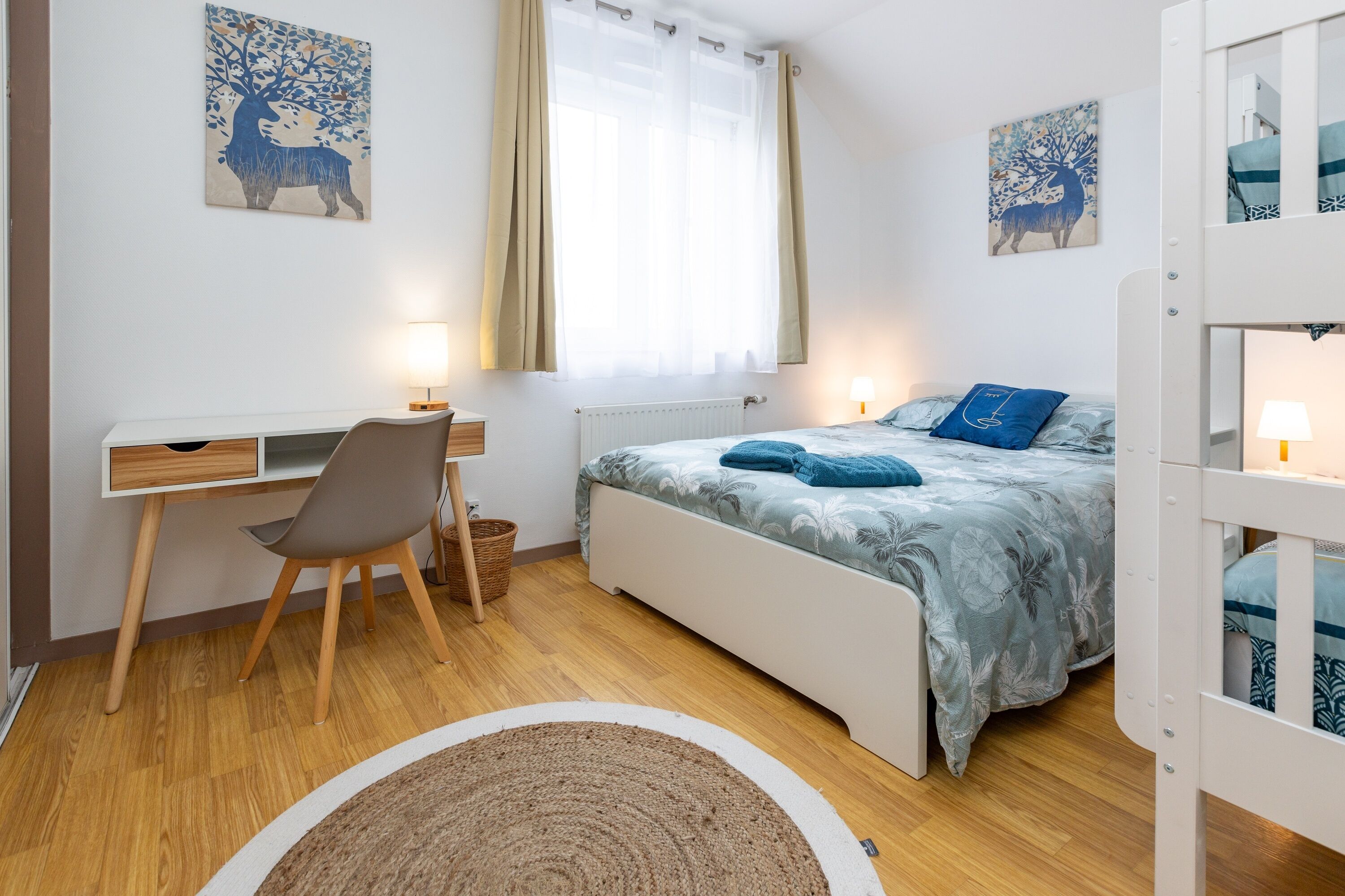 A bedroom with a bed, desk, chair, and a window with curtains.