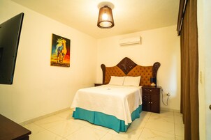 Un dormitorio con cama, mesita de noche, lámpara, un cuadro y un equipo de aire acondicionado.