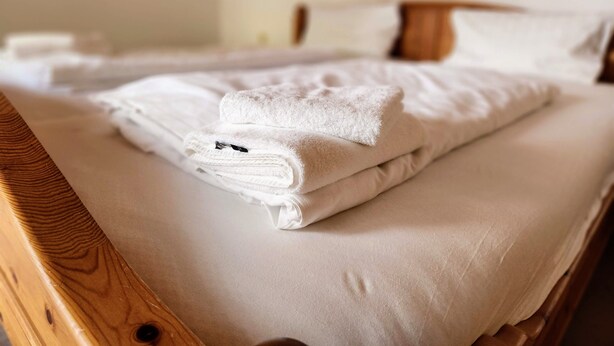 Un lit bien fait, avec du linge de lit blanc et une tête de lit en bois.