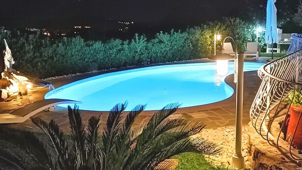 Vue nocturne d’une piscine, avec les meubles de jardin et les aménagements paysagers qui l’entourent.