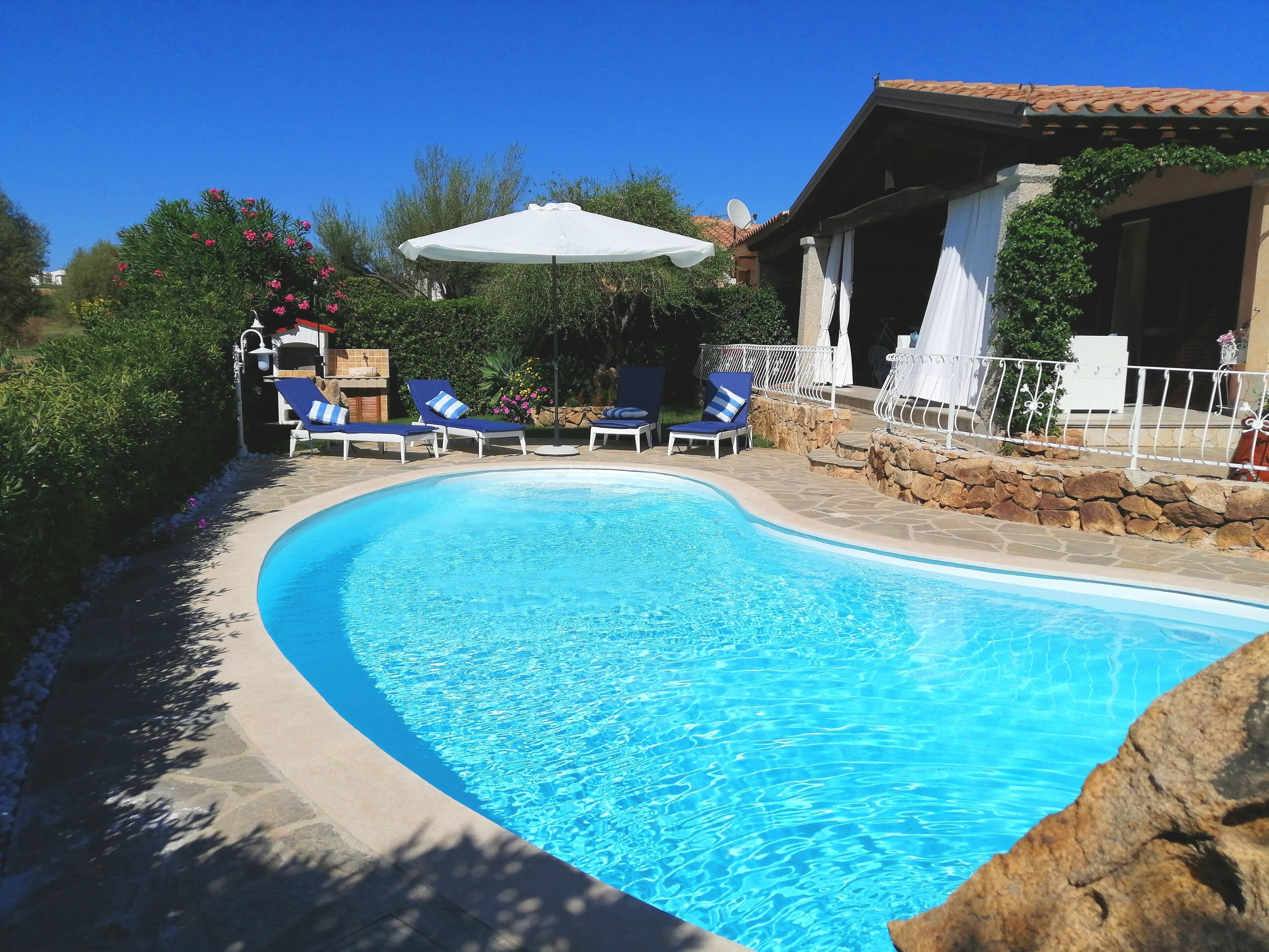 Ein Swimmingpool mit blauem Wasser, umgeben von Liegestühlen und Sonnenschirmen.