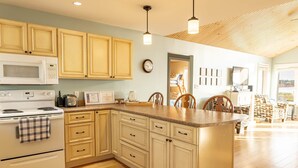 A kitchen with wooden cabinets, a microwave, a stove, and a breakfast bar. - Waterfront Cottage in Stanley Bridge—Bay Views, Sleeps 8, Near Cavendish (North Rustico)
