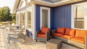 A covered deck with wicker furniture and a blue exterior wall. - Waterfront Cottage in Stanley Bridge—Bay Views, Sleeps 8, Near Cavendish (North Rustico)