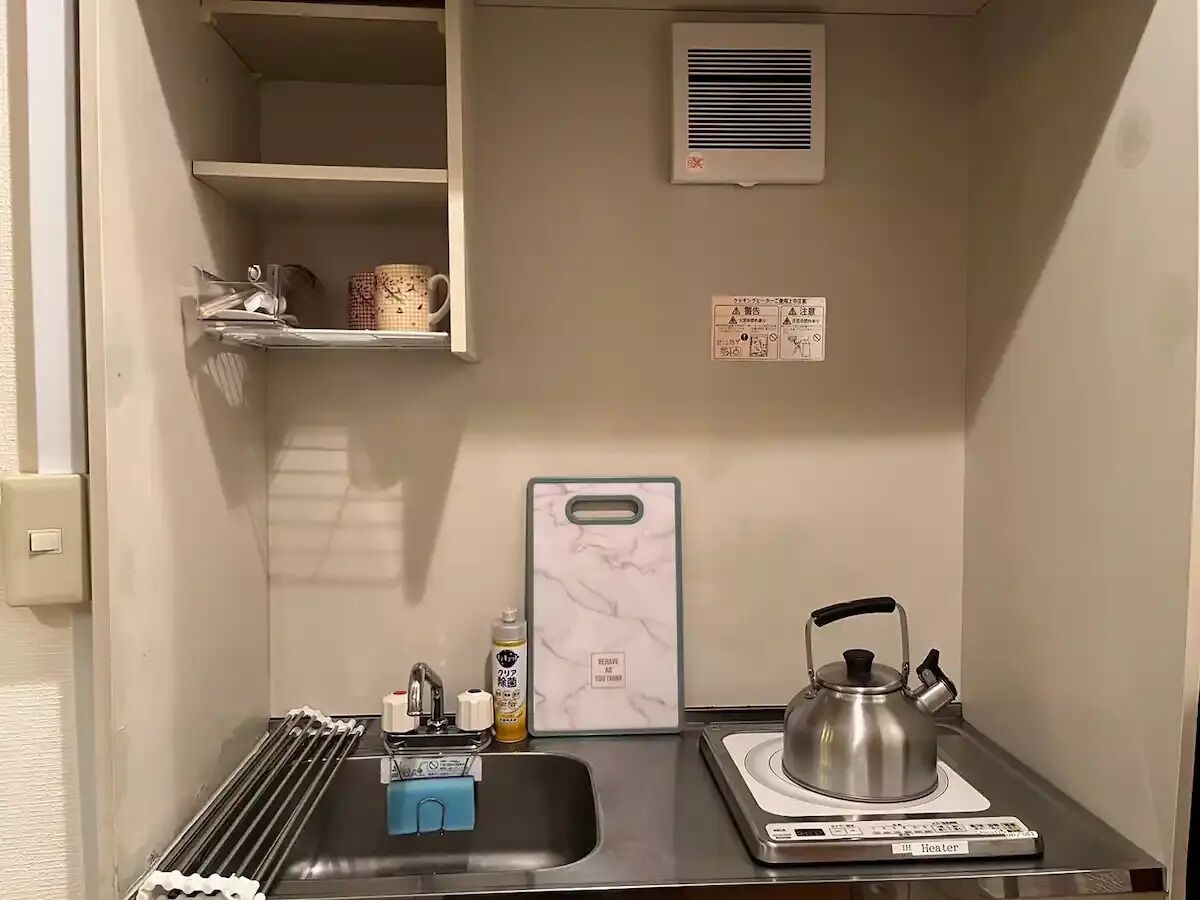 A compact kitchenette with a gas stove, kettle, and a small shelf with a mug.