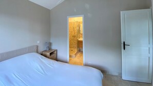 A bedroom with a bed, bedside table, lamp, and a door leading to a bathroom. - Coline's house pool view (Lamonzie-Montastruc)