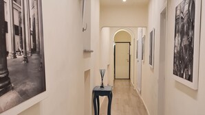 A hallway with a wooden floor, a small table with a vase, and framed artwork on the walls.