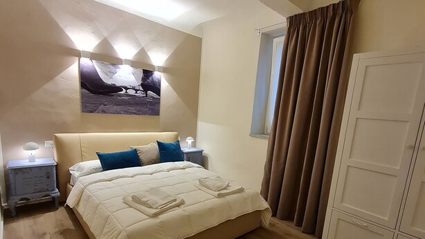 A bedroom with a bed, a nightstand, a chair, a wardrobe, and a window with curtains.