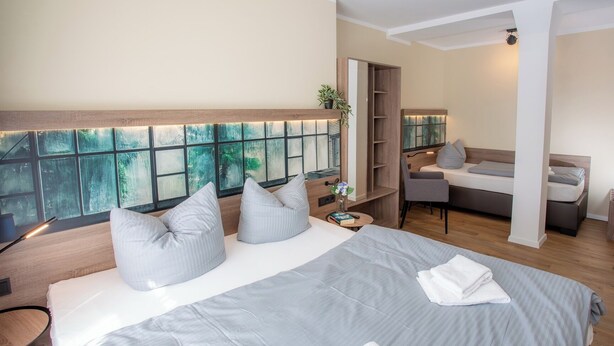 Camera d'hotel moderna con un letto grande, un'area salotto e vista attraverso una finestra con un motivo decorativo.