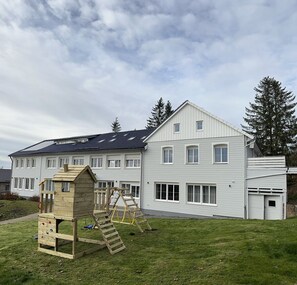 A two-story house with a large front yard, a wooden playhouse, and a ladder.