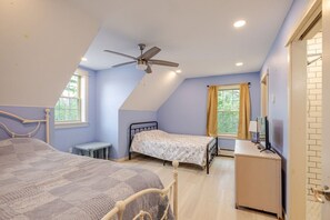 A bedroom with two beds, a ceiling fan, a desk, and a window with curtains.