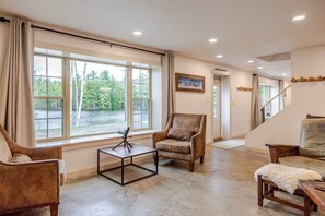 A spacious living room with large windows, a comfortable leather armchair, a wooden coffee table, and a staircase leading to another level.