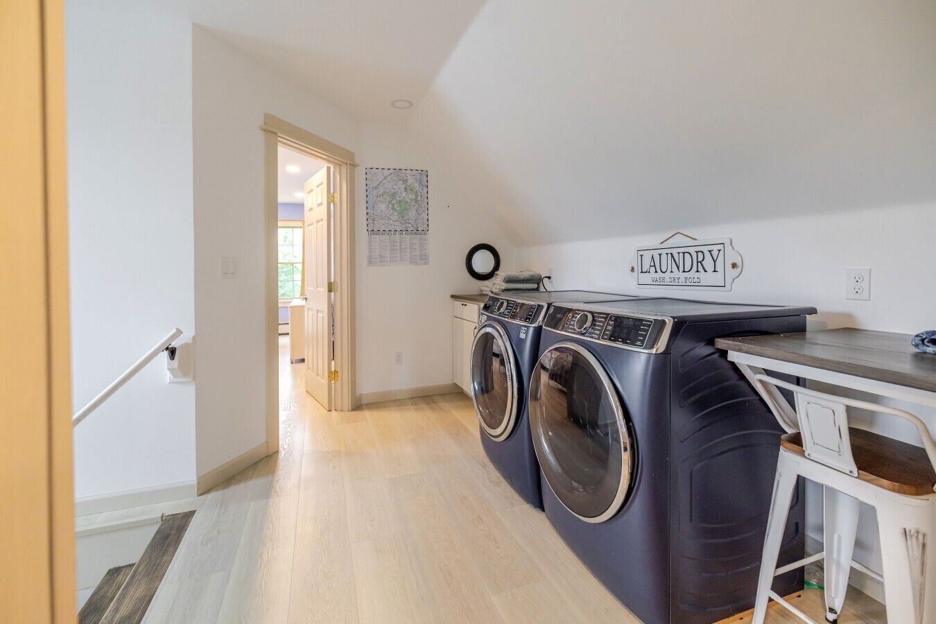 A laundry area with two front-loading washing machines, a drying rack, and a table with a sign that reads 'LAUNDRY'.