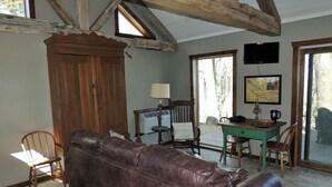 Una habitación rústica con vigas de madera a la vista, un sofá de cuero, un armario de madera, una mesa de comedor con sillas y un televisor montado en la pared.