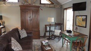 Una sala de estar acogedora con un sofá de cuero marrón, un mueble de madera, una mesa de comedor con sillas y un televisor montado en la pared.