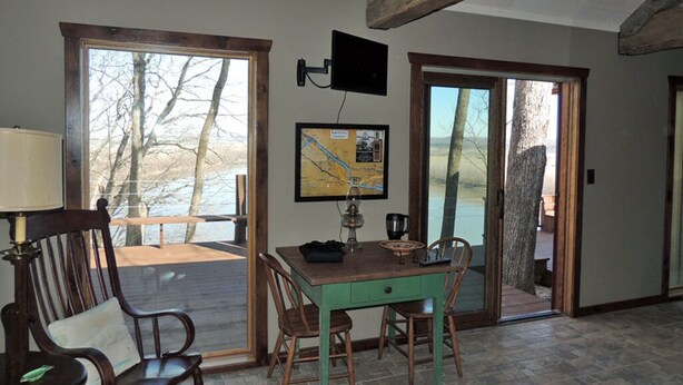 Una habitación con una mesa y sillas de madera, un mapa en la pared y ventanas amplias que dan a una masa de agua.