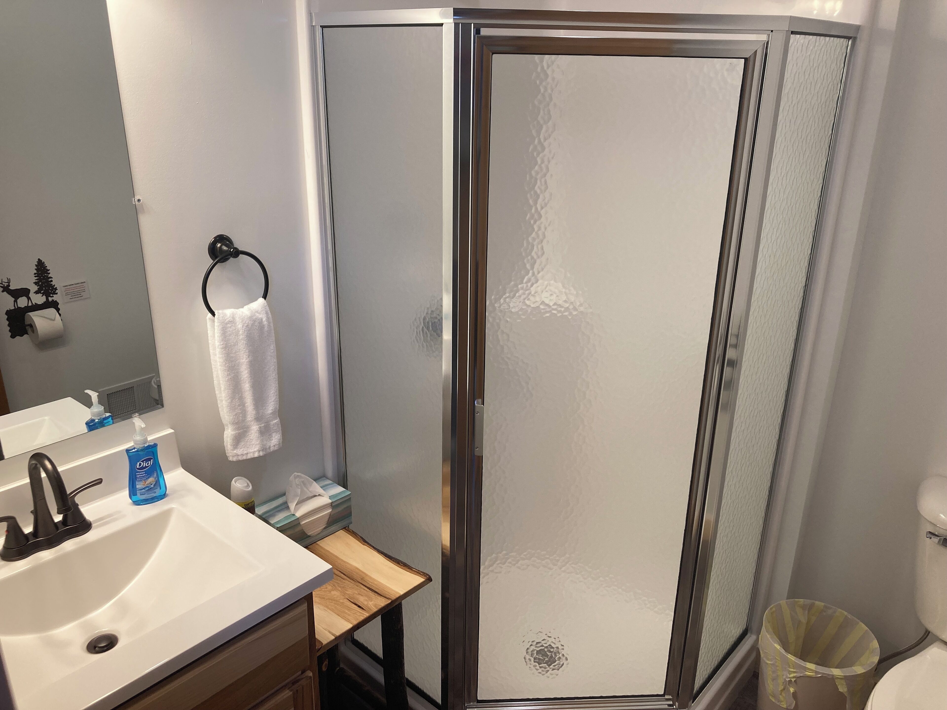 A bathroom with a white sink, a mirror, a towel rack, a shower enclosure, and a toilet.