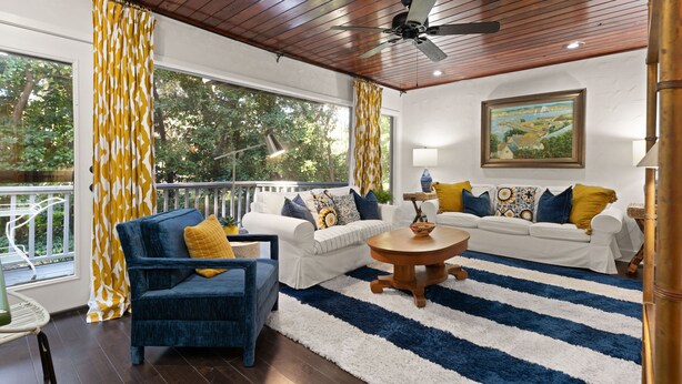 A living room with a blue sofa, white sofas, a wooden coffee table, and yellow and white patterned curtains.