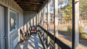 Une véranda couverte avec des balustrades en bois, d’où l’on peut admirer un court de tennis et des arbres.