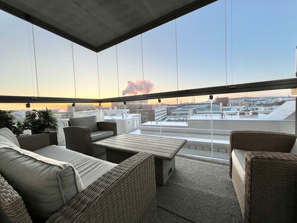 Ein Balkon mit Korbmöbeln, Blick auf die Stadt und ein Sonnenuntergang.
