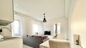 Uma sala de estar moderna e bem iluminada, com um sofá, uma mesa de jantar e uma televisão.