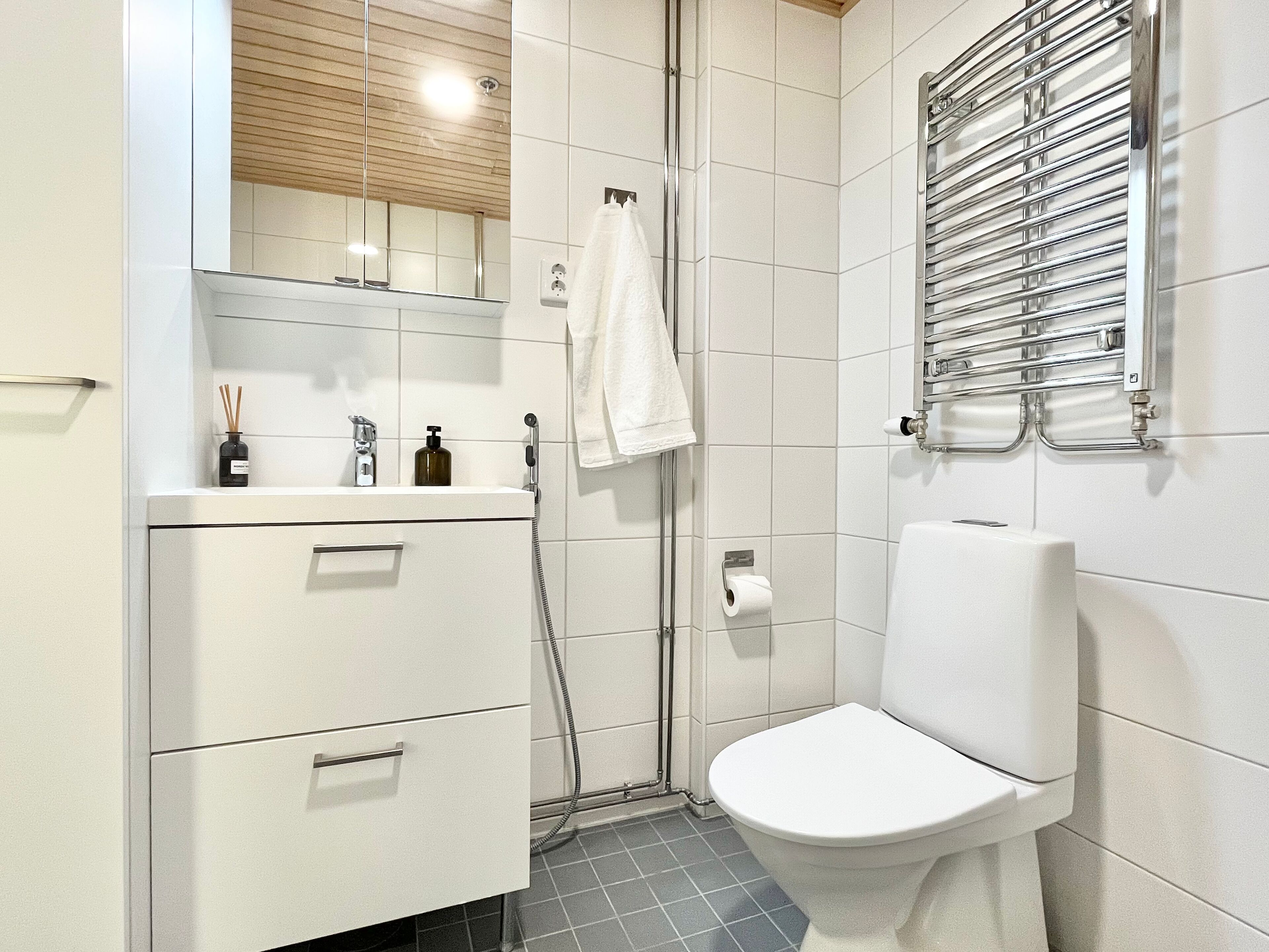 Et moderne badeværelse med toilet, håndvask med spejl, et håndklæde på væggen og en bruseniche.