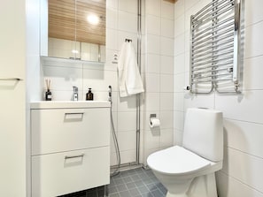A modern bathroom with a toilet, a sink with a mirror, a towel hanging on the wall, and a shower area.