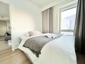 Ein modernes Hotelzimmer mit einem ordentlich bezogenen Bett, einem Fenster mit Vorhängen und Blick auf das Gebäude gegenüber.