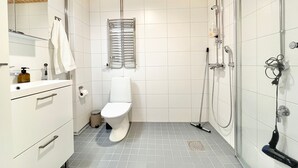 Uma casa de banho moderna com sanita, lavatório, espelho, chuveiro e chão em azulejo.