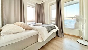 Quarto de hotel moderno com cama, cortinas, ventilador e vista para a cidade.