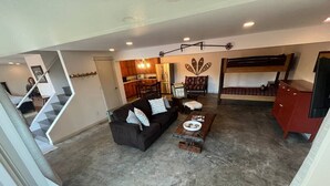 Amplia sala de estar con un sofá marrón oscuro, una mesa de centro y un mueble de aparador rojo. Se ve, al fondo, una cocina con armarios de madera y una mesa de comedor.