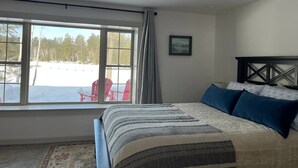Un dormitorio con un ventanal grande, una cama con ropa de cama estampada y vistas a sillas exteriores y nieve.