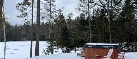 A wooden hot tub with two red Adirondack chairs in a snowy forest setting.