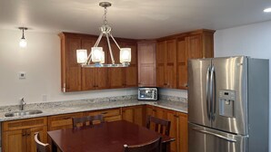 Una cocina con gabinetes de madera, un refrigerador de acero inoxidable, una encimera de granito, una mesa de comedor con sillas y una araña.
