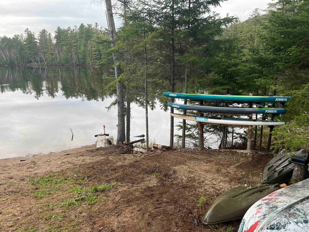 Ein Steg mit einem grünen Kajak und einem Kanu, umgeben von Bäumen und einem ruhigen See.