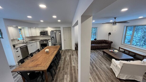 A modern kitchen with a wooden dining table, built-in appliances, and a cozy seating area with a sofa and bench. - Adirondack Wolf Pond Oasis (Lake Placid)