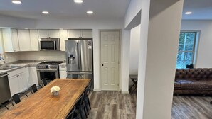 A modern kitchen with white cabinets, stainless steel appliances, and a wooden dining table. - Adirondack Wolf Pond Oasis (Lake Placid)