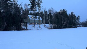 A snow-covered landscape with a house in the background and a child in a snow tube. - Adirondack Wolf Pond Oasis (Lake Placid)