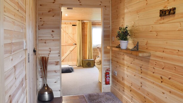 A wooden interior hallway with a rug, a vase with reeds, and a small shelf with a plant. - 2 bedroom accommodation in West Walton (West Walton)