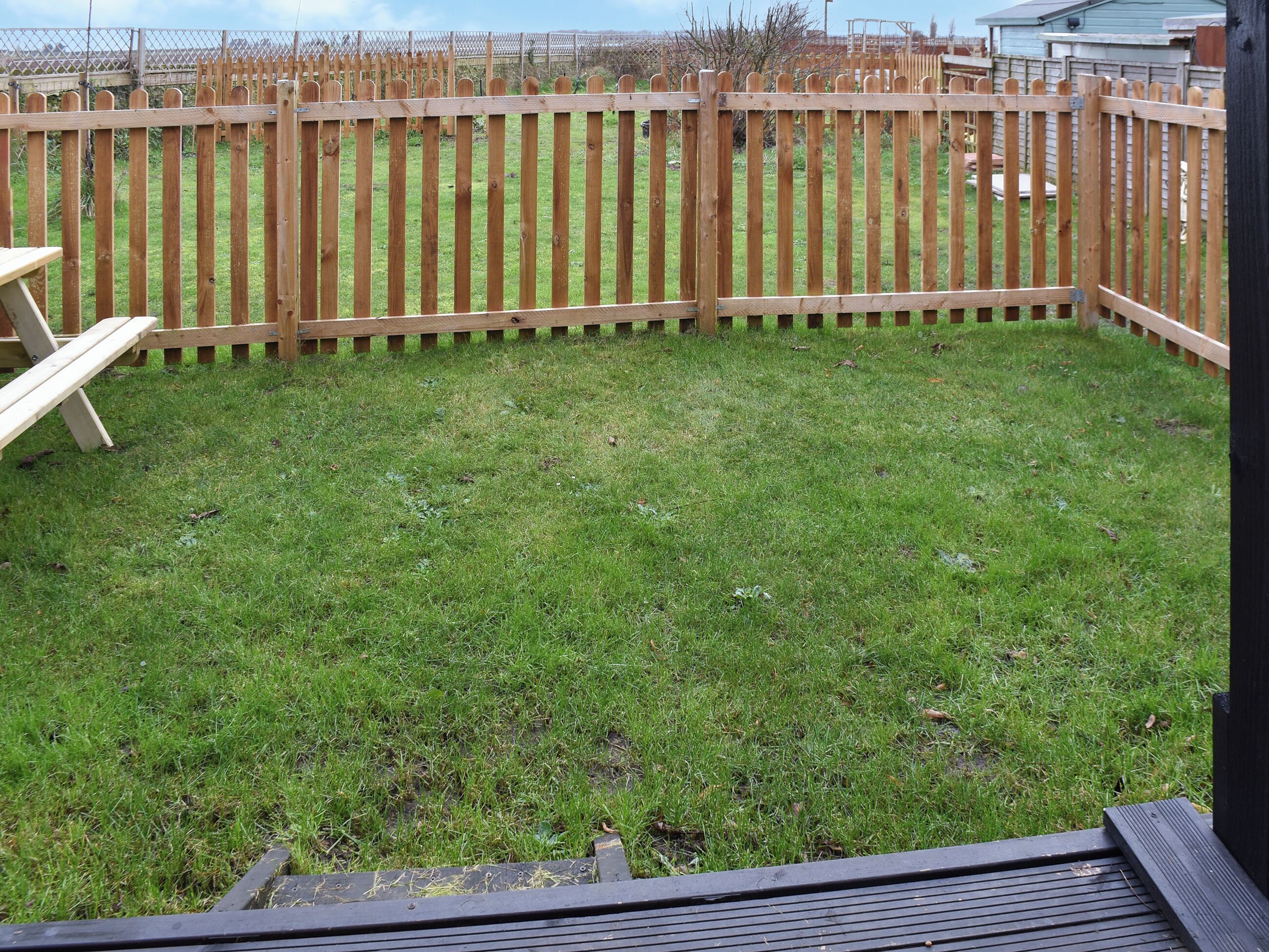 A fenced backyard with a wooden deck and a picnic table.