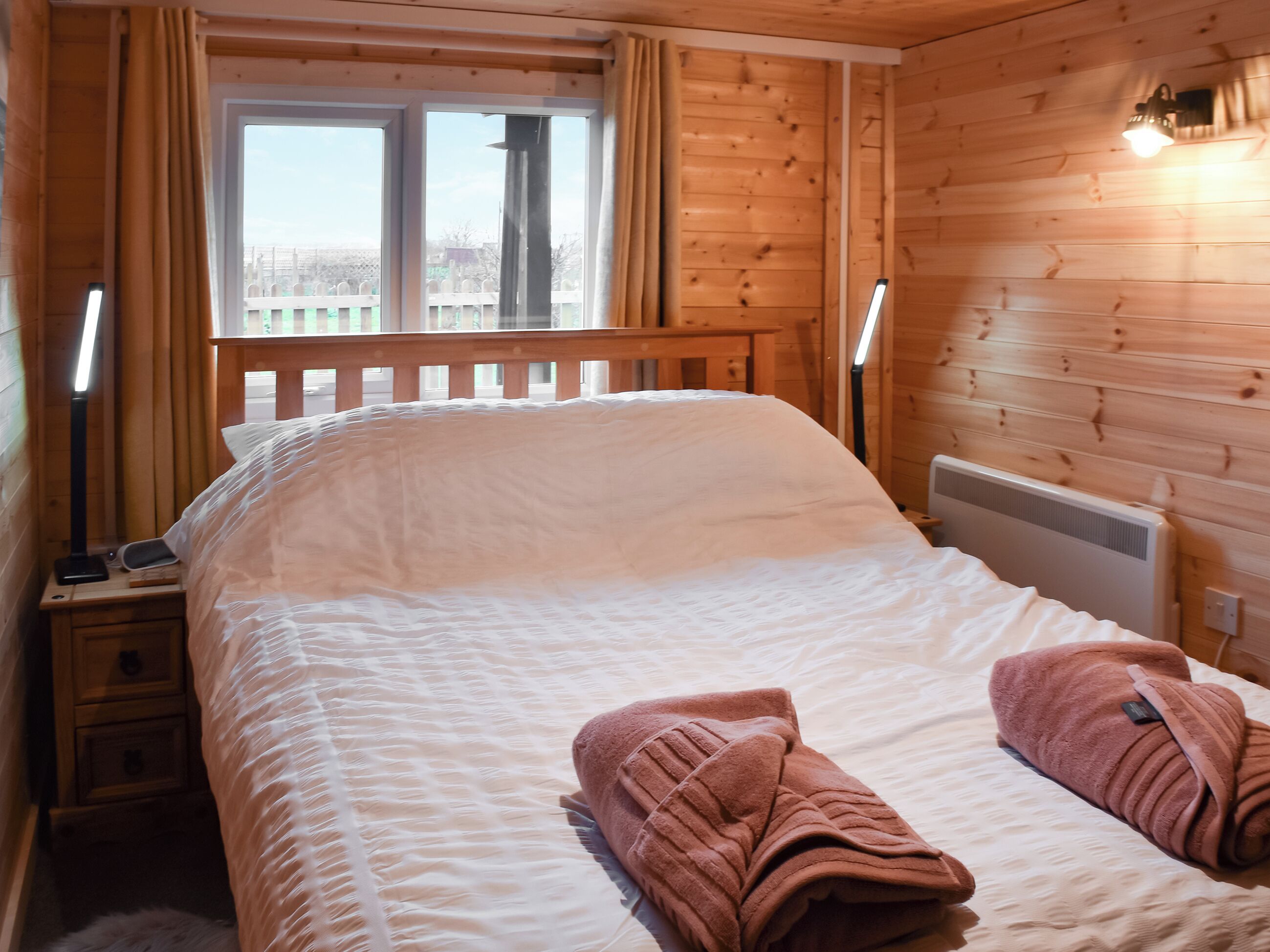 Une chambre dans un chalet en bois, avec un lit, deux lampes de chevet, une fenêtre et un radiateur.