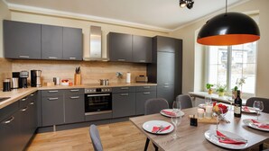 Een moderne keuken met grijze kastjes, een ingebouwde oven en een eethoek voor vier personen met een houten tafel en stoelen.