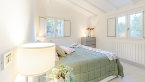 A bedroom with a green bedspread, a bedside lamp, and a vase of flowers.