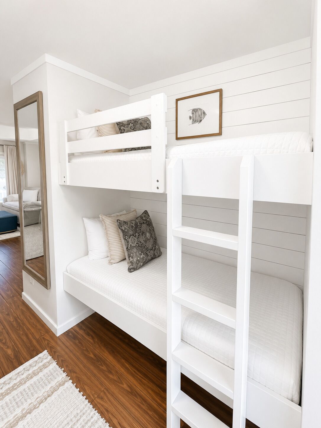 A room with a bunk bed, a sofa, a mirror, and a framed picture on the wall.