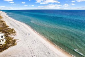 An aerial view of a beach with clear turquoise waters and a sandy shore.