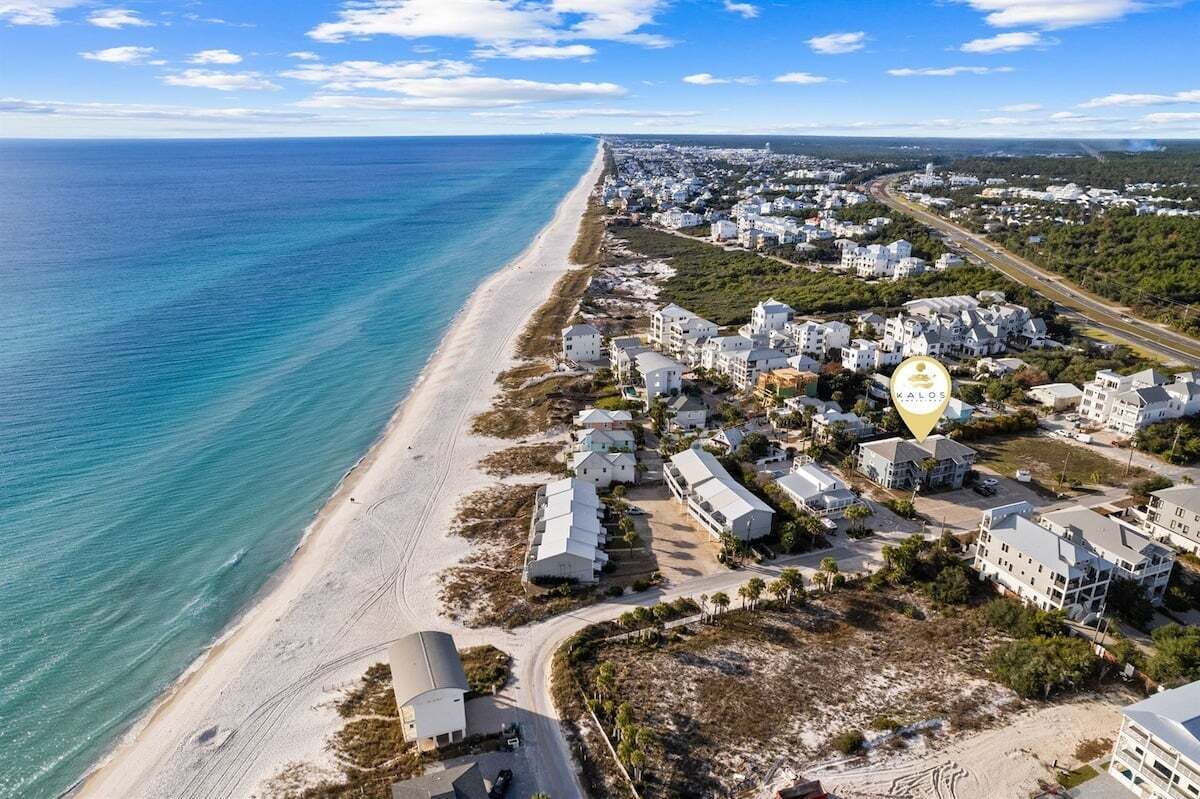 An aerial view of a coastal residential area with a beach, houses, and a prominent building with a golden dome.