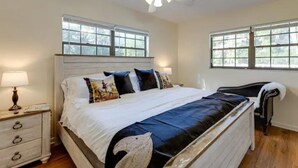 A bedroom with a large bed, two windows, a ceiling fan, and a nightstand with a lamp. - Pennyfarthing Farm South (Ocala)