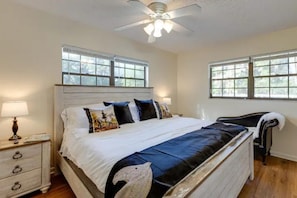 Quarto com cama grande, duas janelas, ventoinha no teto e mesa de cabeceira com abajur.