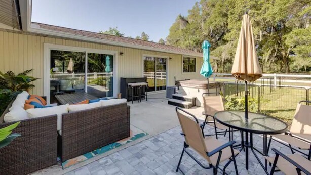 An outdoor patio with wicker furniture, a glass table, and a hot tub. - Pennyfarthing Farm South (Ocala)