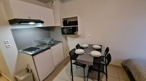 Uma cozinha compacta com fogão, micro-ondas e uma pequena prateleira. Há uma mesa de jantar com cadeiras e pratos dispostos para quatro pessoas.