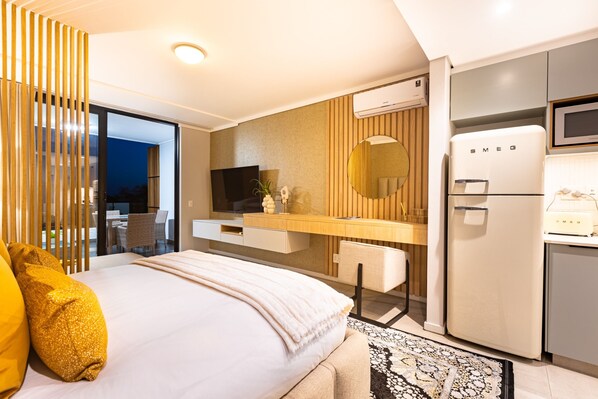 A modern hotel room with a bed, a desk, a flat-screen TV, a refrigerator, and a large window.